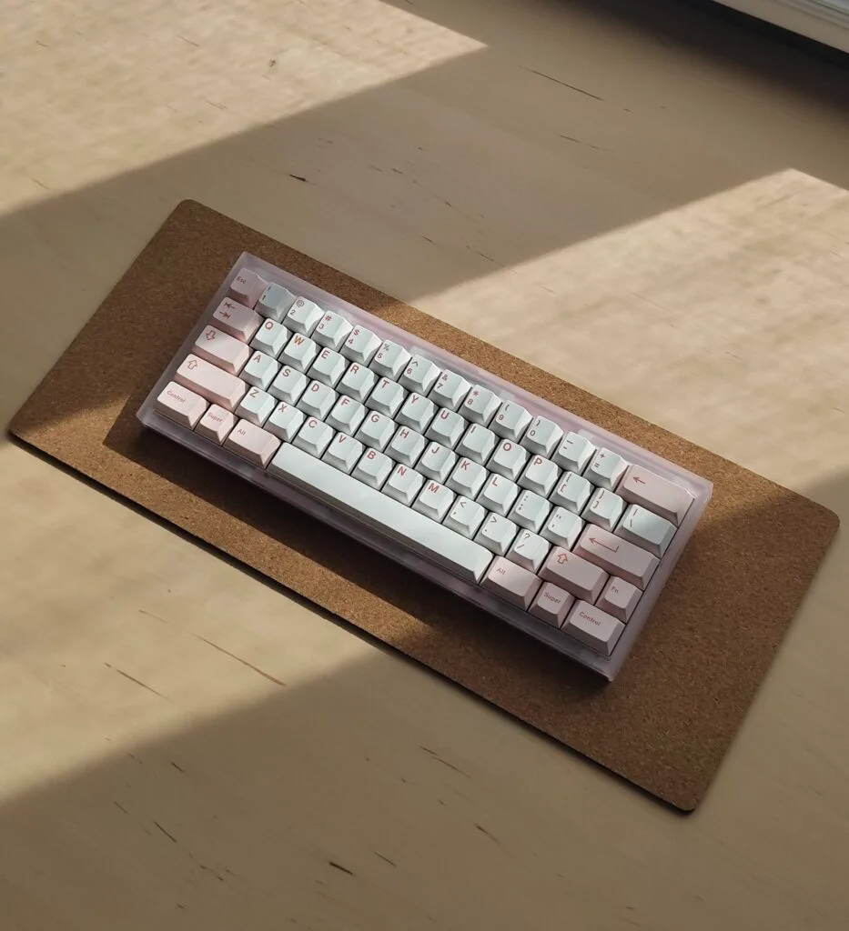 Pink, white and acrylic small keyboard on a cork deskmat